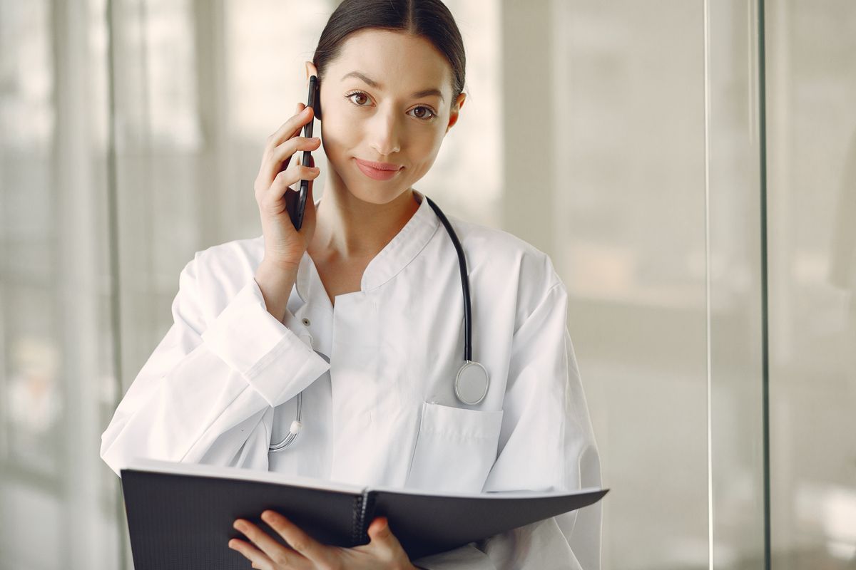A clinician checking patient messages on her phone in a bright clinic hallway