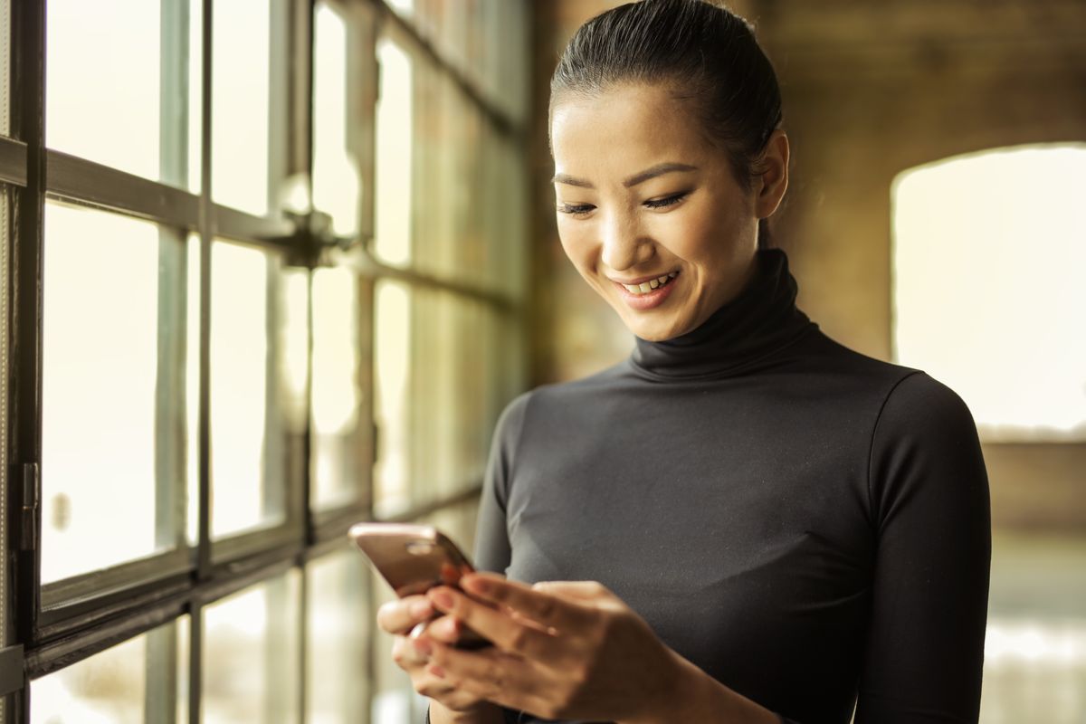A patient smiling as she reads a text from her clinic by a sunny window