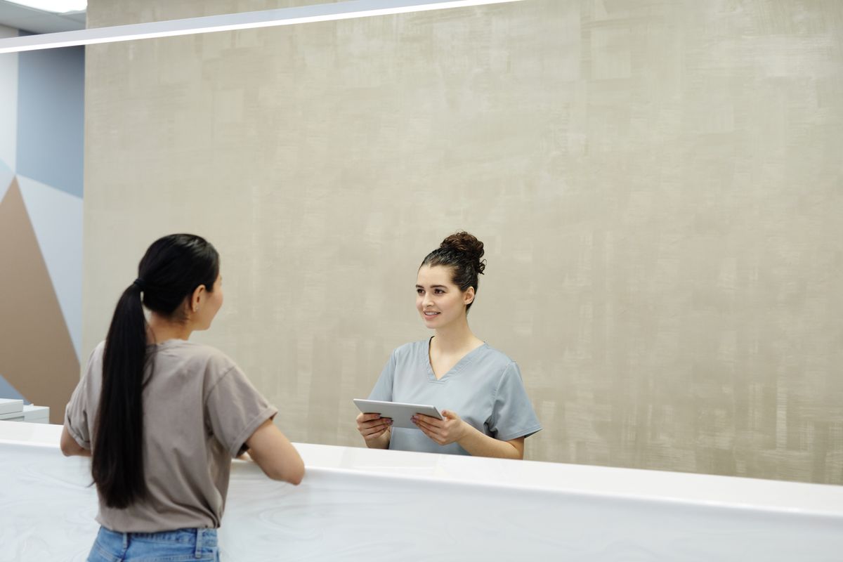 A front-desk team member with a tablet welcoming a patient at a bright clinic reception
